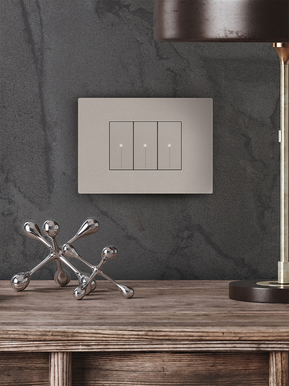 BTicino Light Now 3-module light switch in sand stone color, above a wood table with metal decor and a lamp.