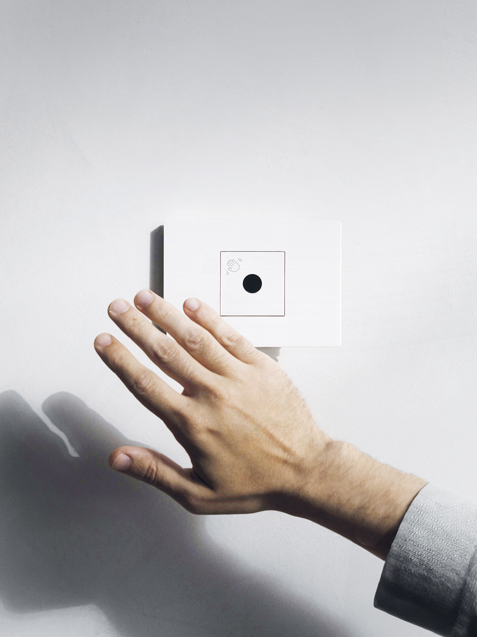 A hand reaches for a white BTicino Light Now wall-mounted switch from the Circular collection, featuring touchless control.