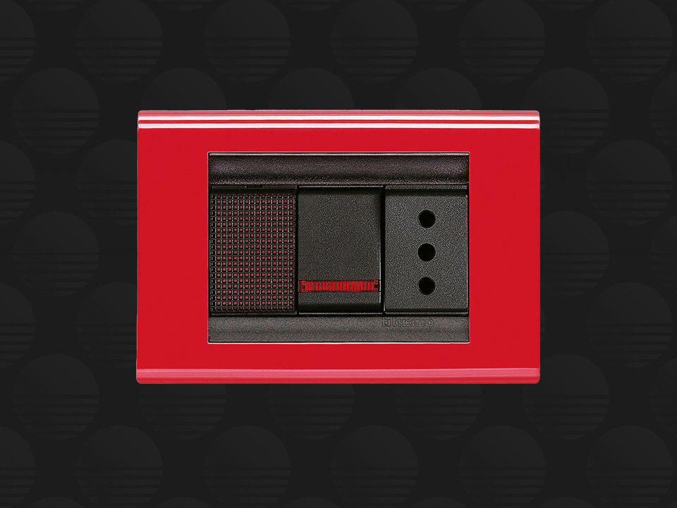 BTicino Living Classic red 3-module cover plate, on a dark patterned background.
