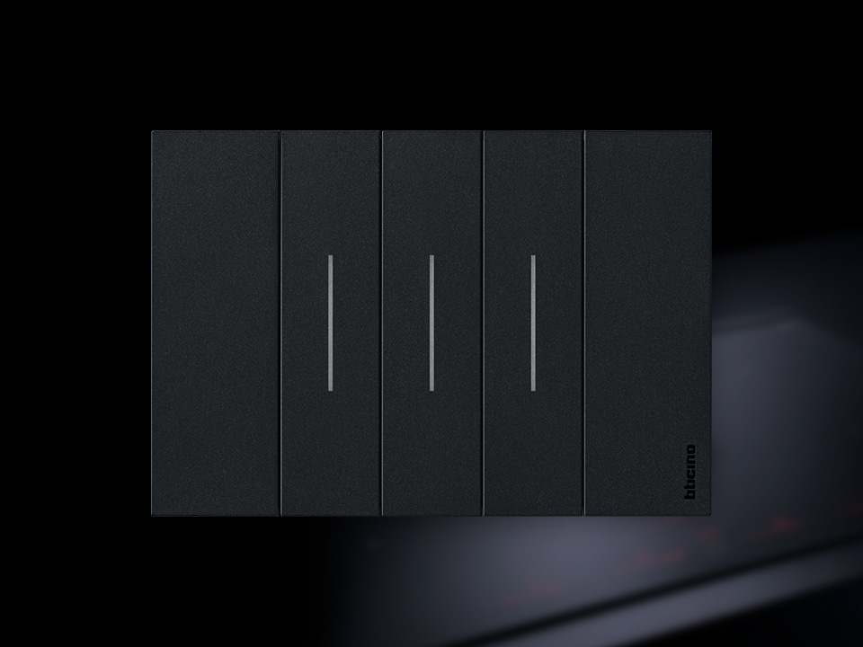 BTicino Living Now black 3-module light switch, on a black blurry background.