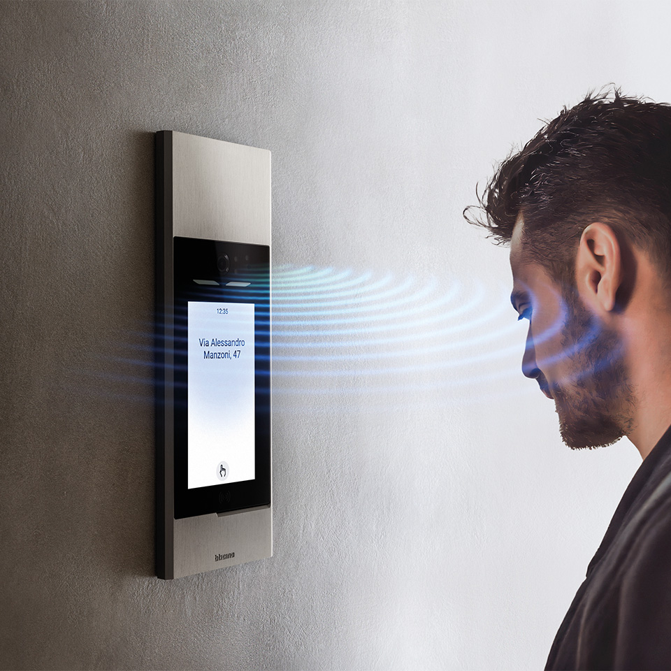 A man uses the BTicino Linea 5000 wall-mounted facial recognition system with proximity sensor and digital screen.