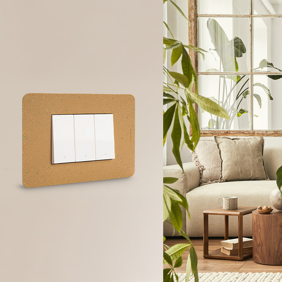 BTicino MatixGO with bio cover plate mounted on a beige wall, in the background a living room with plants, a sofa, and a wooden coffee table.