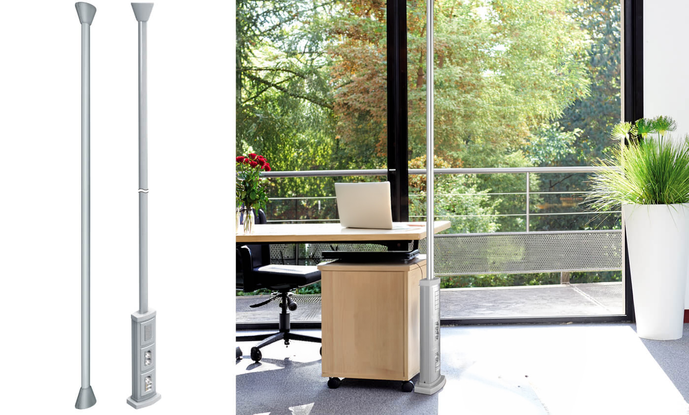 A low-voltage power supply column with single-sided sockets is installed next to a desk in a modern office with large windows.