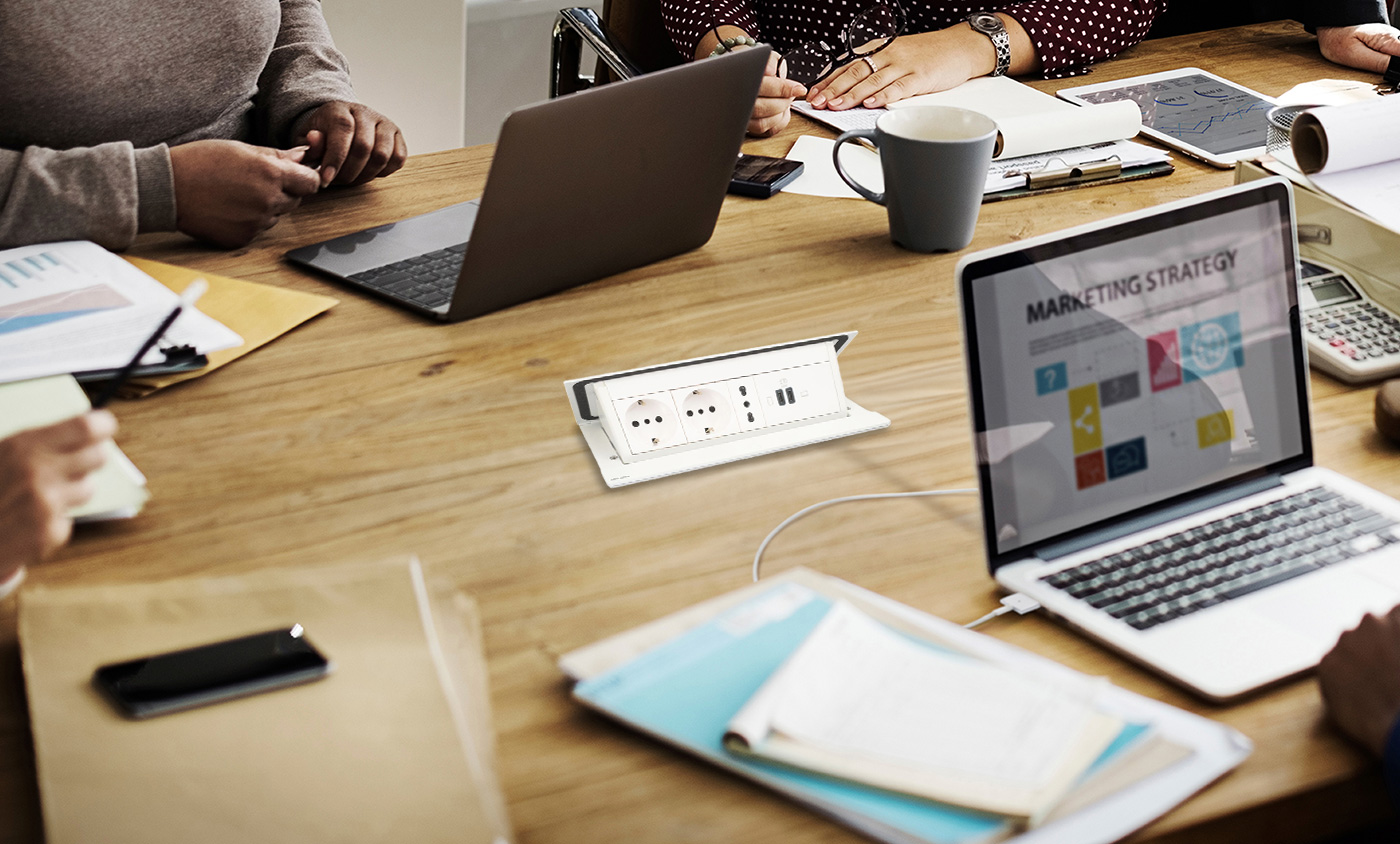 Some people are using laptops whilst sitting at a table fitted with a BTicino 150482NW Pop-up Turret.